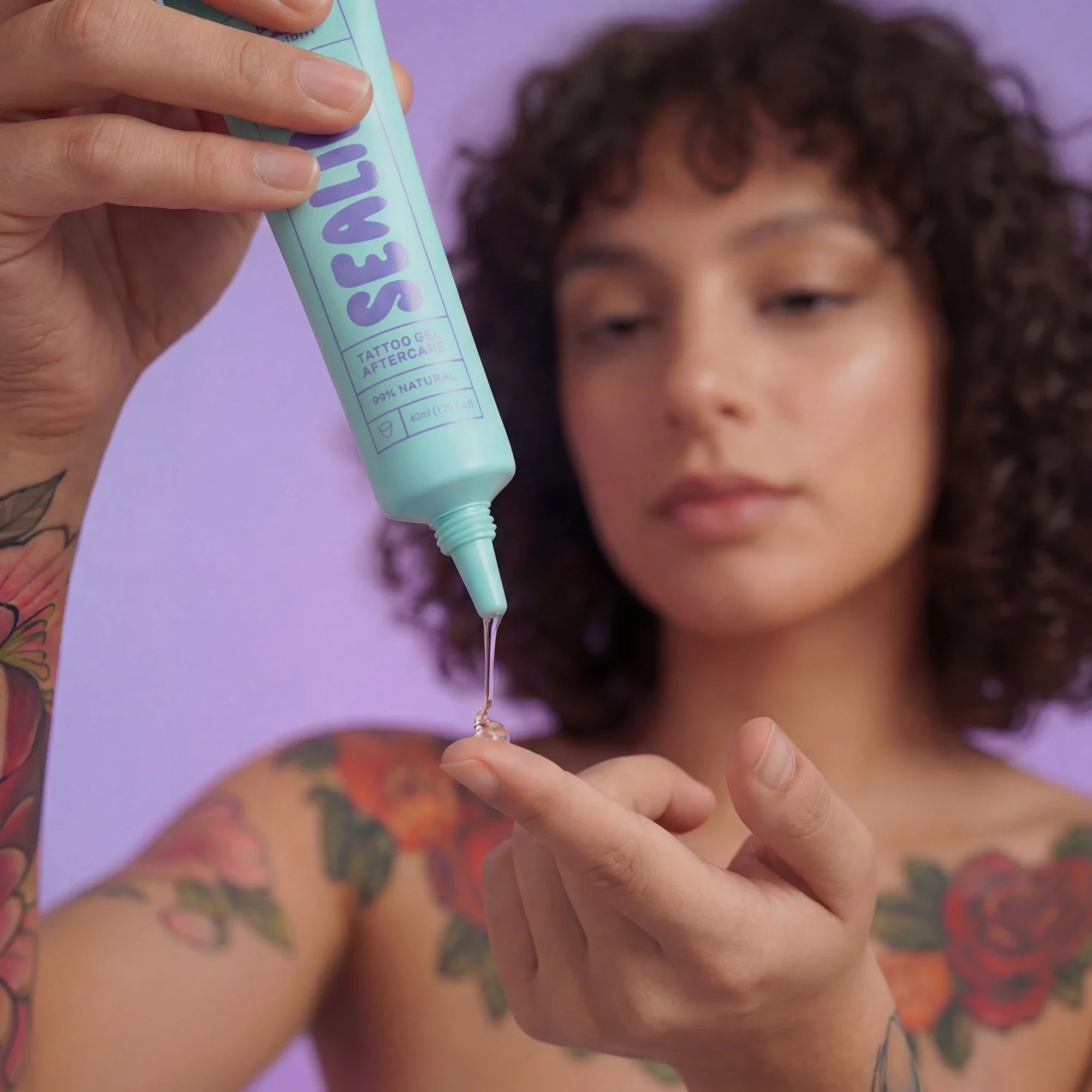 Person applying tattoo aftercare product to their arm with a purple background