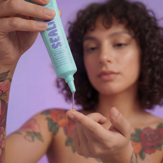 Person applying tattoo aftercare product to their arm with a purple background